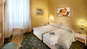 A hotel room with two beds, a chair, a desk, and a lamp.
