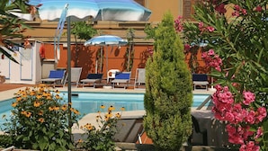 A pool area with lounge chairs and umbrellas, surrounded by flowers and greenery.
