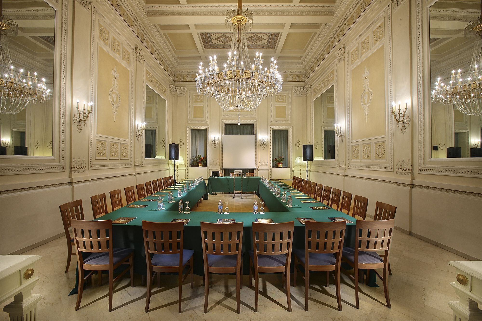 A formal meeting room with a long table, chairs, chandeliers, and ornate wall decorations.