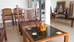 A living room with wooden furniture, a glass coffee table with fruit, and a Buddha statue. - Empyrean Hotel (Seeduwa - Katunayake)