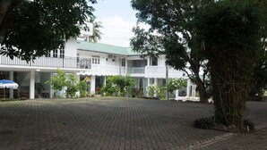 A courtyard with a paved walkway, surrounded by a white building with multiple balconies and a covered area. - Empyrean Hotel (Seeduwa - Katunayake)