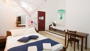 A hotel room with a bed, a desk, a chair, a mirror, and a mosquito net. - Empyrean Hotel (Seeduwa - Katunayake)