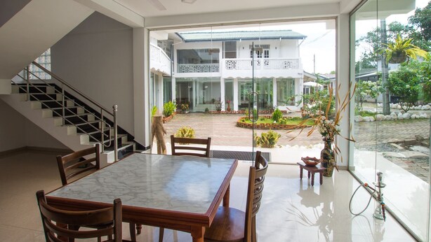 A modern interior with a dining area, a staircase, and a view of a courtyard with a building. - Empyrean Hotel (Seeduwa - Katunayake)