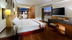 A hotel room with a large bed, a desk with a flat-screen TV, a chair, and a view of the city at dusk. - Cheng Pao Hotel (Puli)