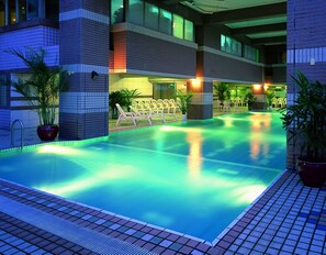 A swimming pool with a tiled edge, surrounded by lounge chairs and potted plants, with a building featuring a modern design in the background. - Cheng Pao Hotel (Puli)