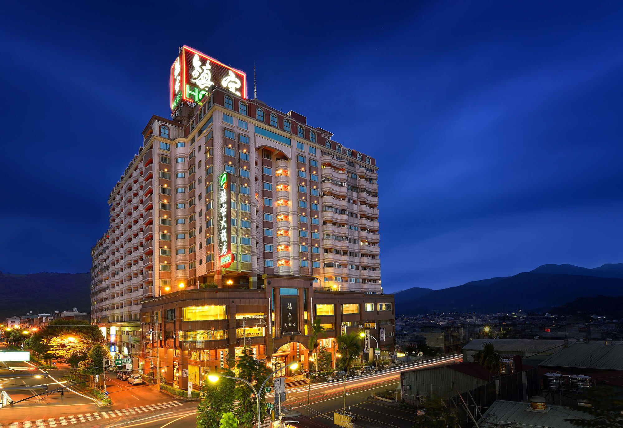 A multi-story hotel with a prominent sign at the top, multiple balconies, and a view of the surrounding cityscape.