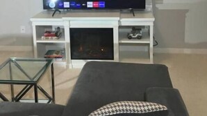 A living room with a flat-screen TV on a white stand, a grey sofa, and a glass coffee table. - Royal Castle Suites  (Edmonton)