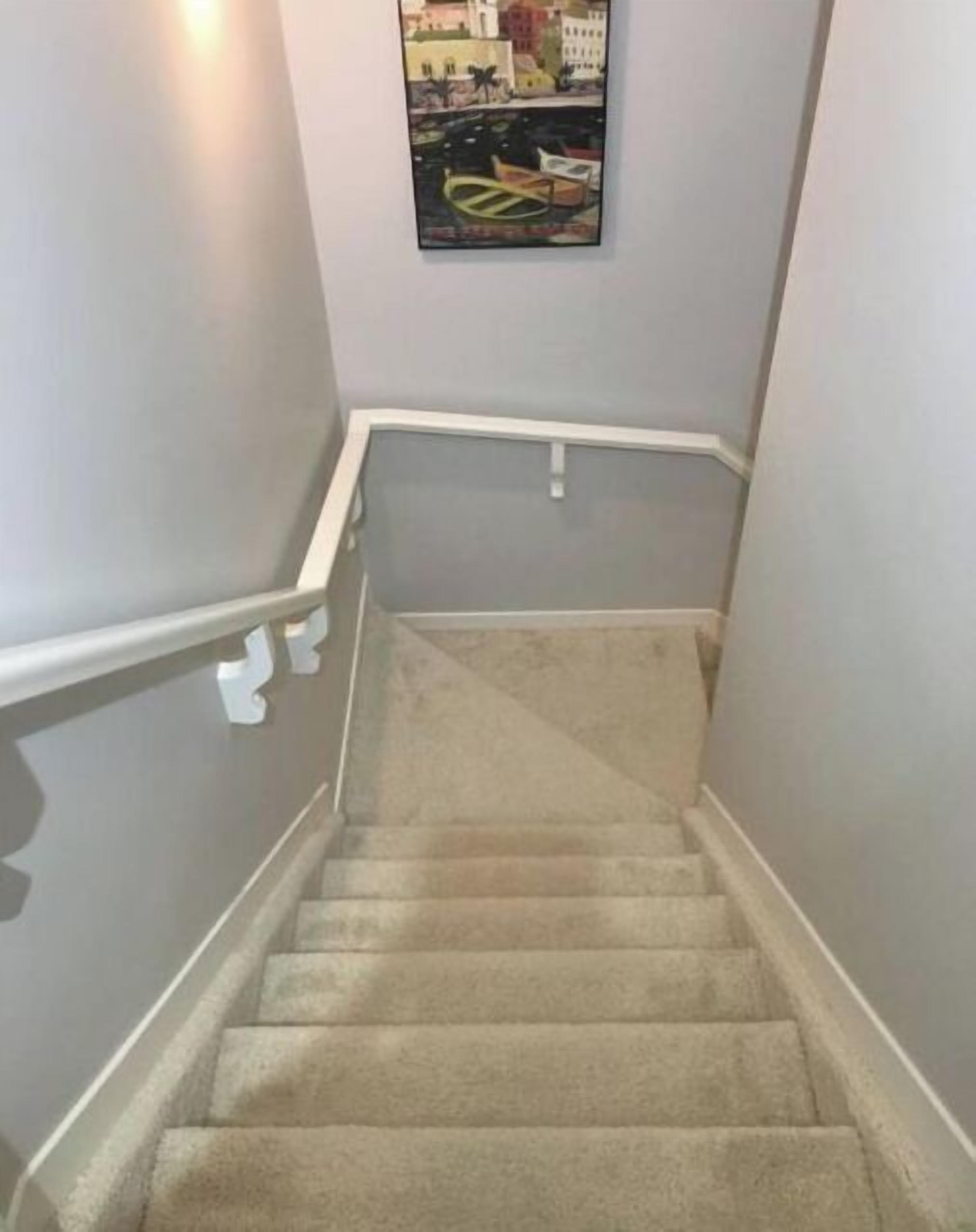 A carpeted staircase with white handrails and a picture of a cityscape on the wall above.