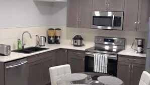 A modern kitchen with grey cabinets, a microwave, a stove, and a sink. There is a round dining table with two chairs. - Royal Castle Suites  (Edmonton)