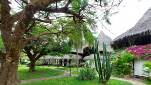 A lush garden with thatched-roof huts, a pathway, and a variety of plants and cacti. - Harbour Key Cottages (Malindi)