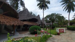 A courtyard with thatched-roof huts, palm trees, and a stone pathway. - Harbour Key Cottages (Malindi)