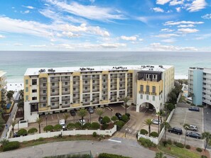A multi-story hotel with balconies, a parking area, and a view of the ocean.