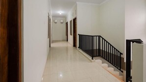 A clean, well-lit hallway with a tiled floor, a black railing on the right, and doors leading to other rooms.