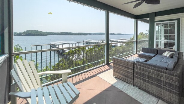 A balcony with a view of a body of water, a wicker sofa, and a white Adirondack chair. - HT901 - Impressive lakefront condo! (Lake Ozark)