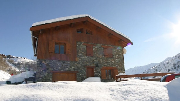 Un bâtiment de style chalet, doté d’une façade en pierre et d’un revêtement extérieur en bois, entouré de collines enneigées.
