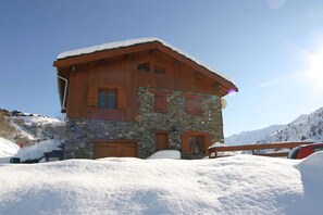 A chalet-style building with a stone facade and wooden exterior, surrounded by snow-covered hills.