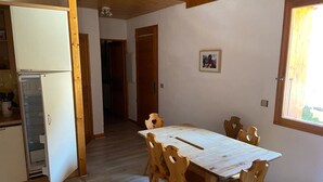 Un coin repas avec une table et des chaises en bois, un réfrigérateur et une fenêtre laissant entrer la lumière naturelle.