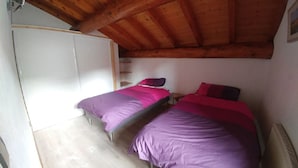 Une chambre avec deux lits, des poutres apparentes en bois au plafond, une armoire blanche et un radiateur.