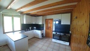 Une cuisine compacte avec des meubles blancs, un plan de travail noir, un four encastré et un plafond en bois.