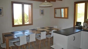 Un coin repas avec une table et des chaises en bois, un comptoir de cuisine et de grandes fenêtres à cadres en bois.