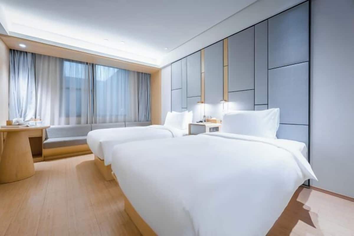 A modern hotel room with a large bed, bedside tables, a desk, and a window with curtains.