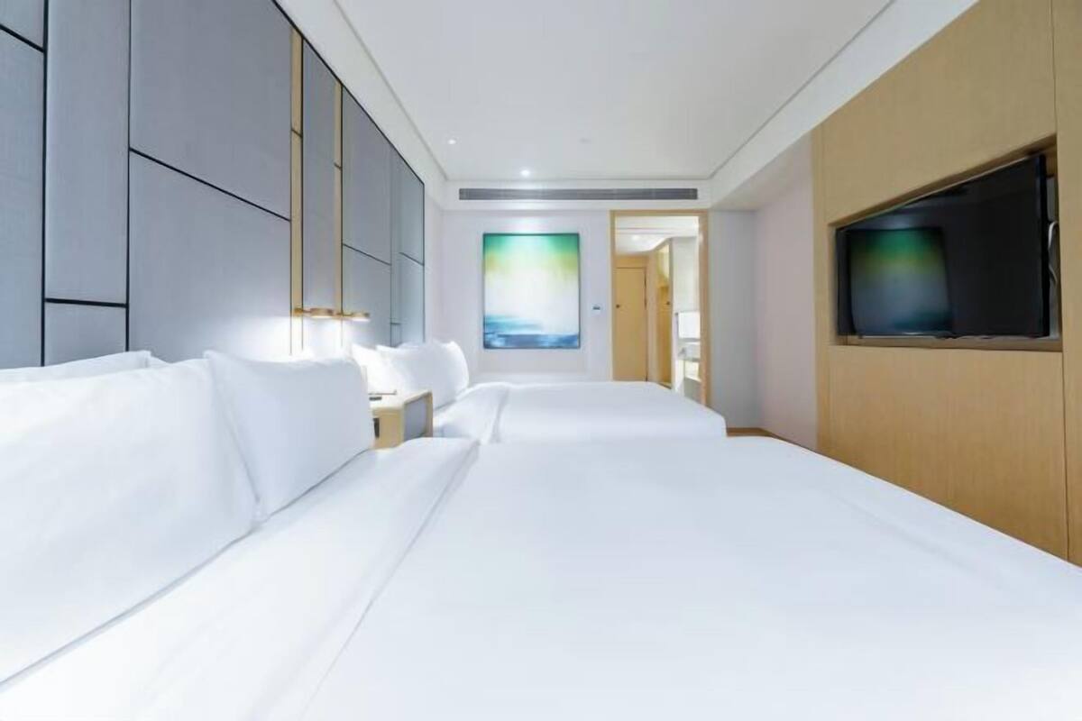 A hotel room with a large bed, a TV mounted on the wall, and a painting on the wall.
