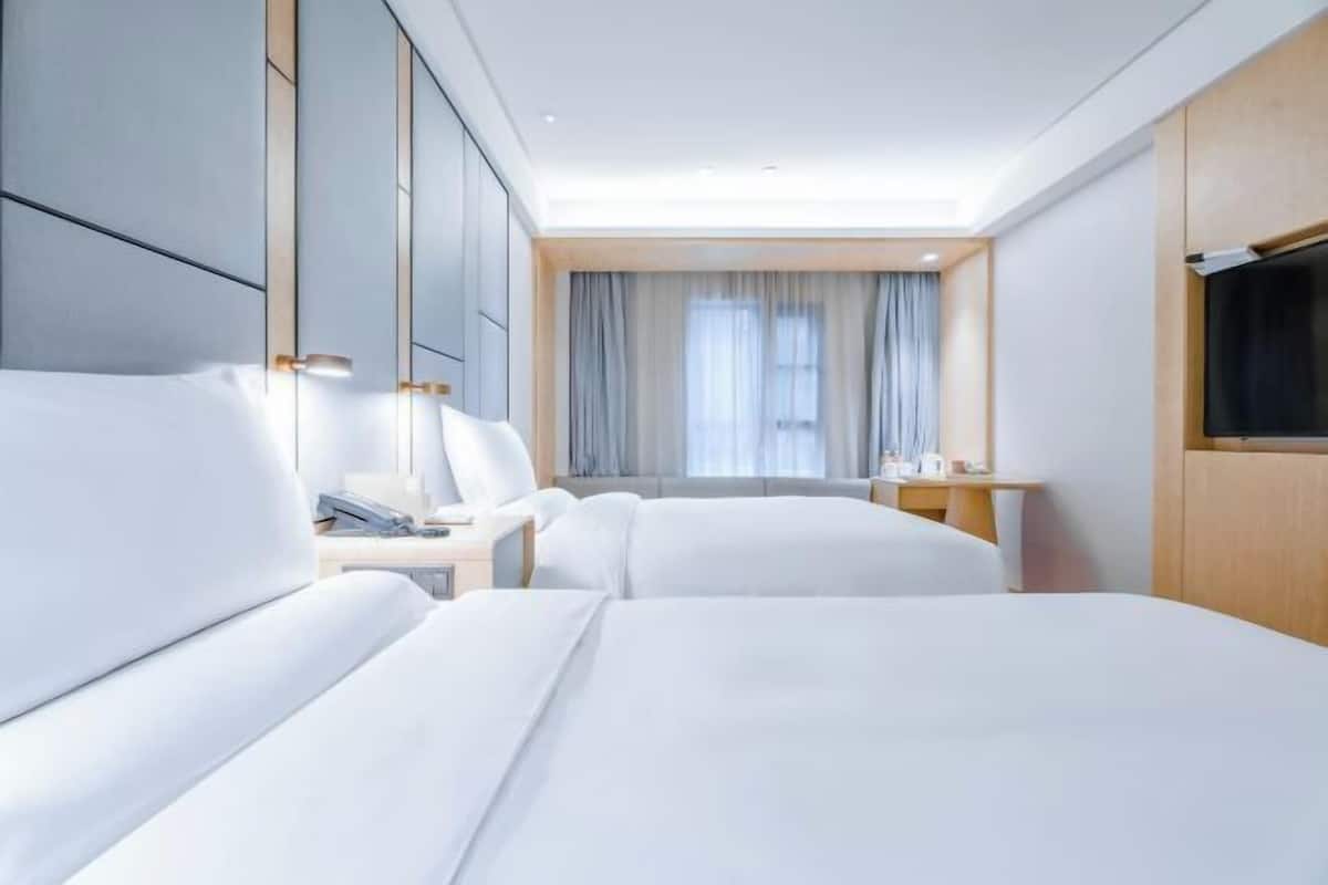 A hotel room with two beds, a desk, a chair, a TV, and a window with curtains.