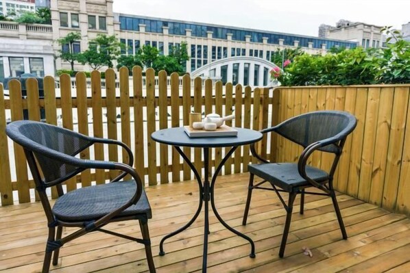 A wooden deck with two wicker chairs and a small round table, featuring a teapot and cups.