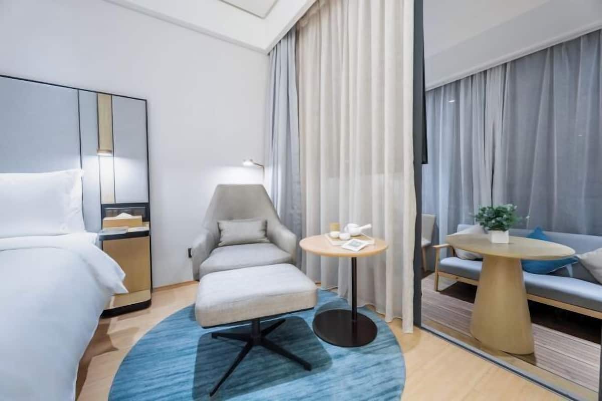 A hotel room with a bed, a desk, a chair, a round table, and a sofa.