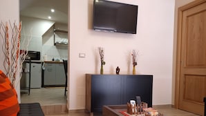Ein modernes Wohnzimmer mit einem an der Wand befestigten Flachbildfernseher, einem dunklen Holztisch mit dekorativen Gegenständen, einem schwarzen Sofa und einer Holztür.