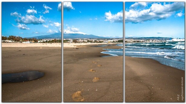 Ein Strand mit Fußspuren, die zum Wasser führen, ein Berg im Hintergrund und ein klarer Himmel.