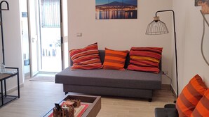Ein modernes Wohnzimmer mit einem grauen Sofa, orangefarbenen Kissenstreifen, einem Holztisch und einer schwarzen Stehlampe.