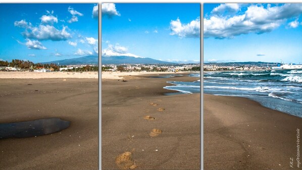 Ein Strand mit Fußspuren, die zum Wasser führen, ein Berg im Hintergrund und ein klarer Himmel.