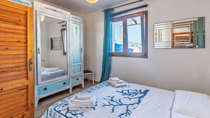 Een slaapkamer met een bed, een kledingkast, een spiegel en een raam met gordijnen.