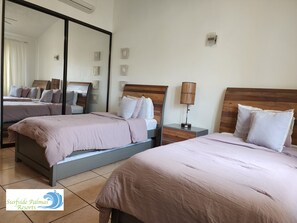 A hotel room with two beds, a large mirror, a bedside table with a lamp, and a wall-mounted light fixture.