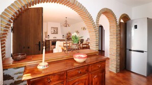 A kitchen with wooden cabinets, a refrigerator, and a dining area with a table and chairs. - 1200 Villa el Barco (Nerja)