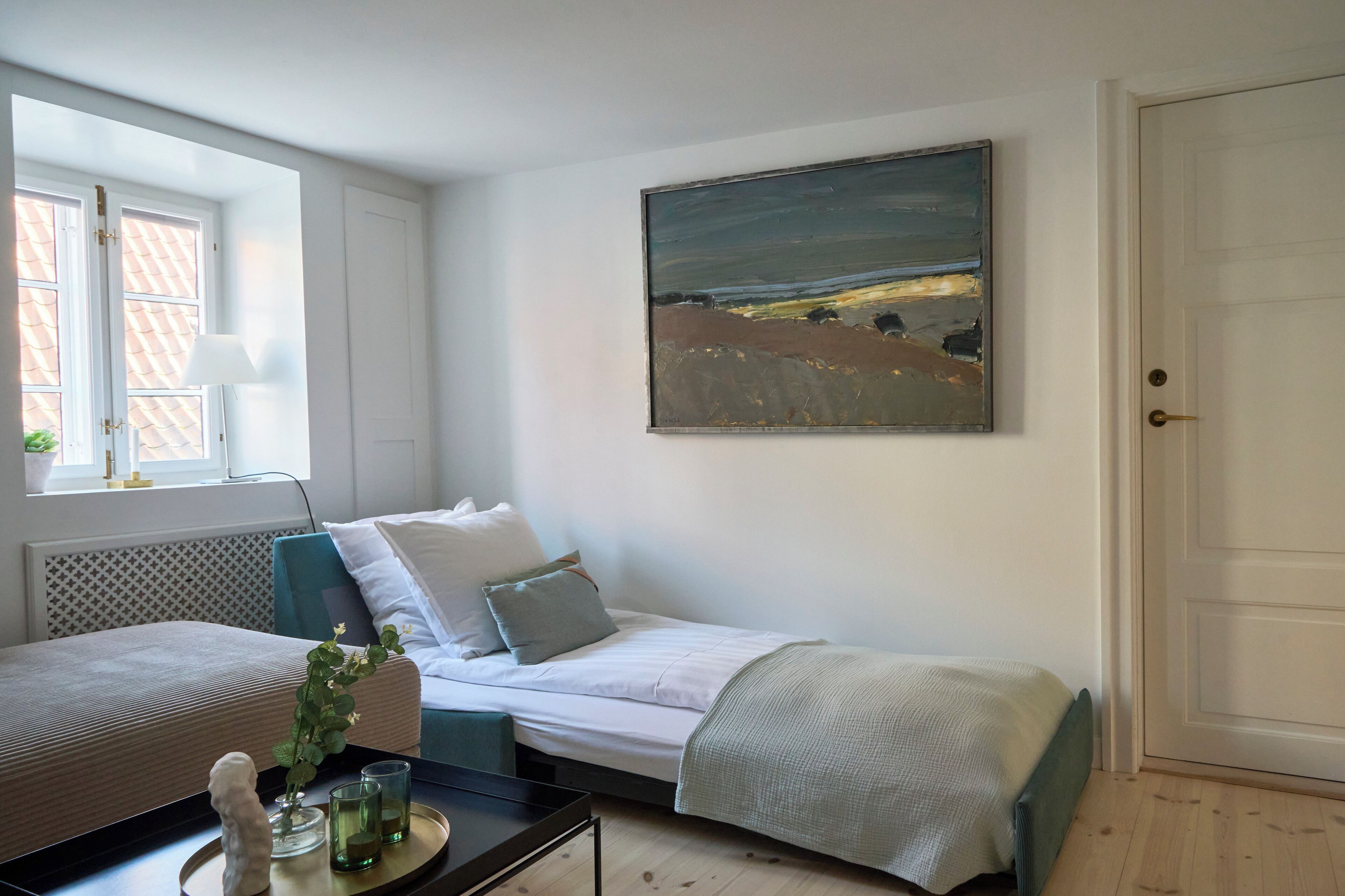 A bedroom with two beds, a window with blinds, a painting on the wall, and a door.