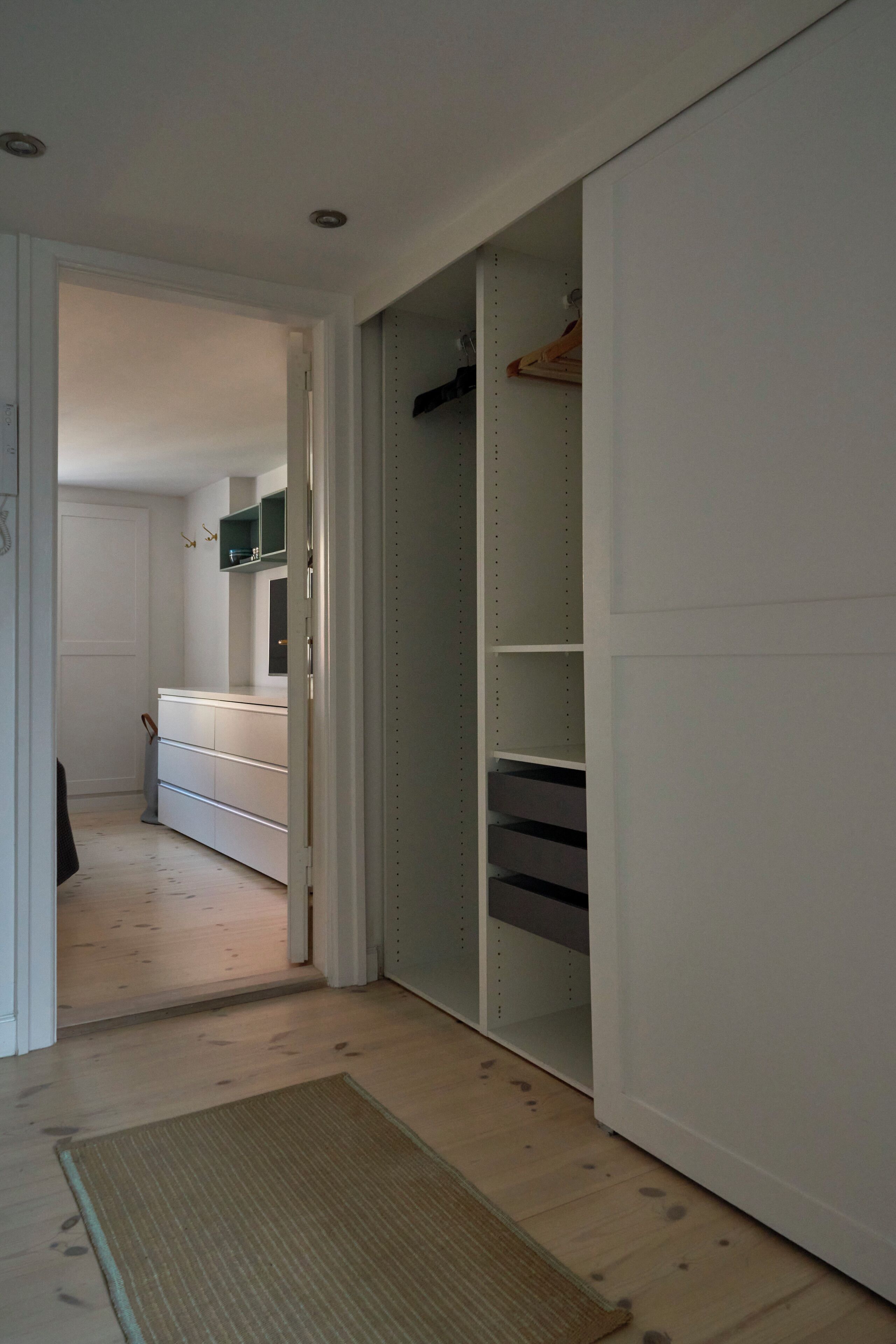 Ein Flur mit Holzboden, der zu einem Schlafzimmer mit Bett und Kleiderschrank führt.