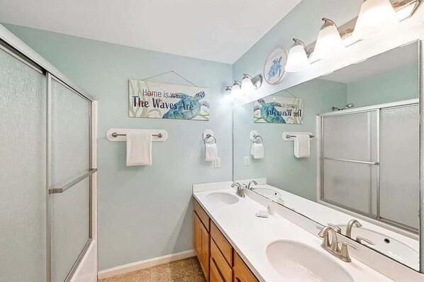A bathroom with a shower, two sinks, a large mirror, and towel racks.