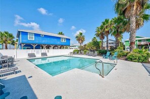 Un'area piscina con un edificio blu, sedie a sdraio e palme.