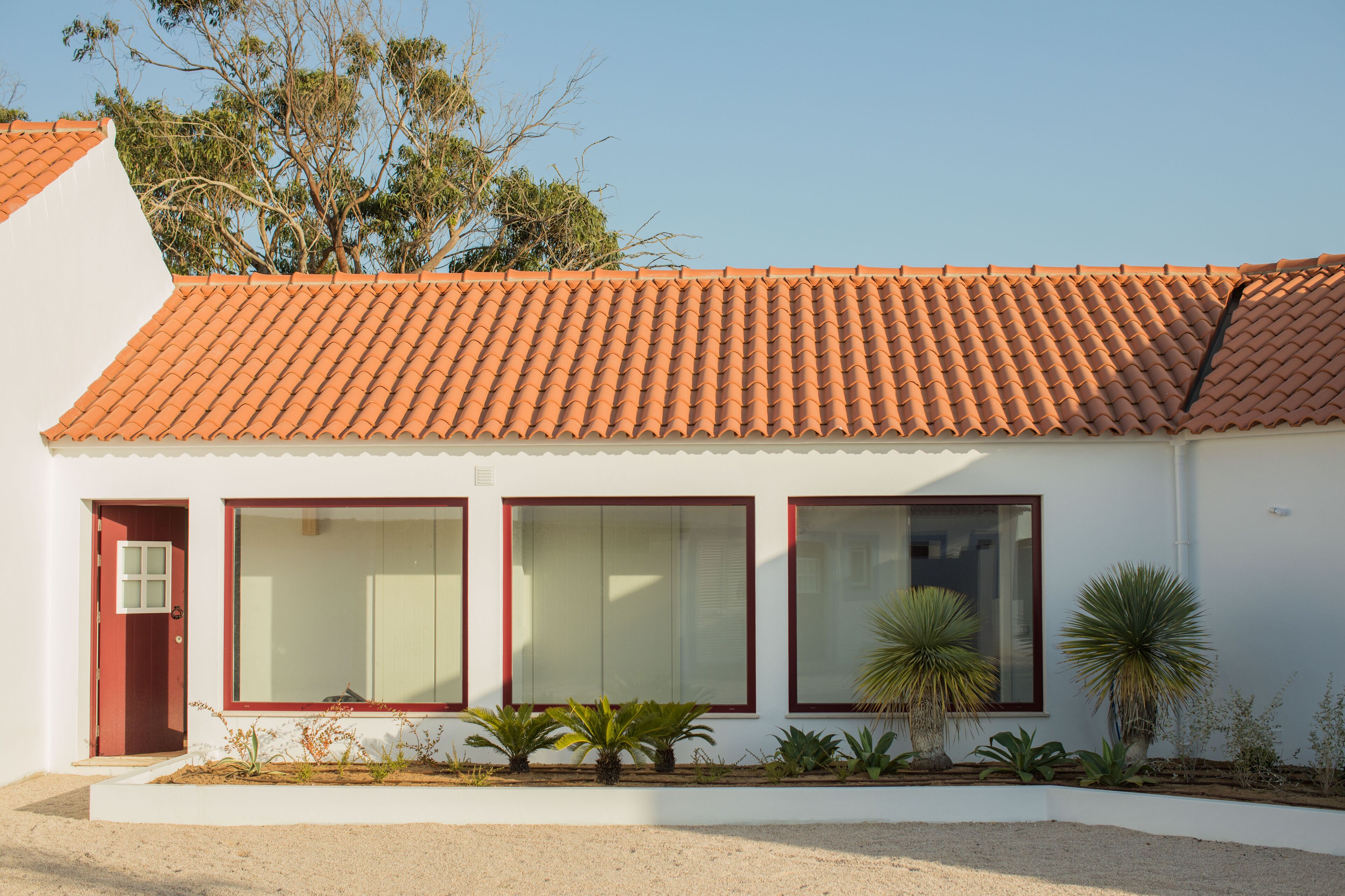Una casa moderna con techo de tejas rojas, ventanas amplias y un pequeño jardín con plantas.