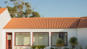 Una casa moderna con techo de tejas rojas, ventanas amplias y un pequeño jardín con plantas.