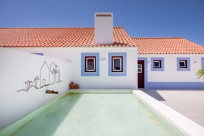 A building with a tiled roof, a swimming pool, and a wall with a simple line drawing.