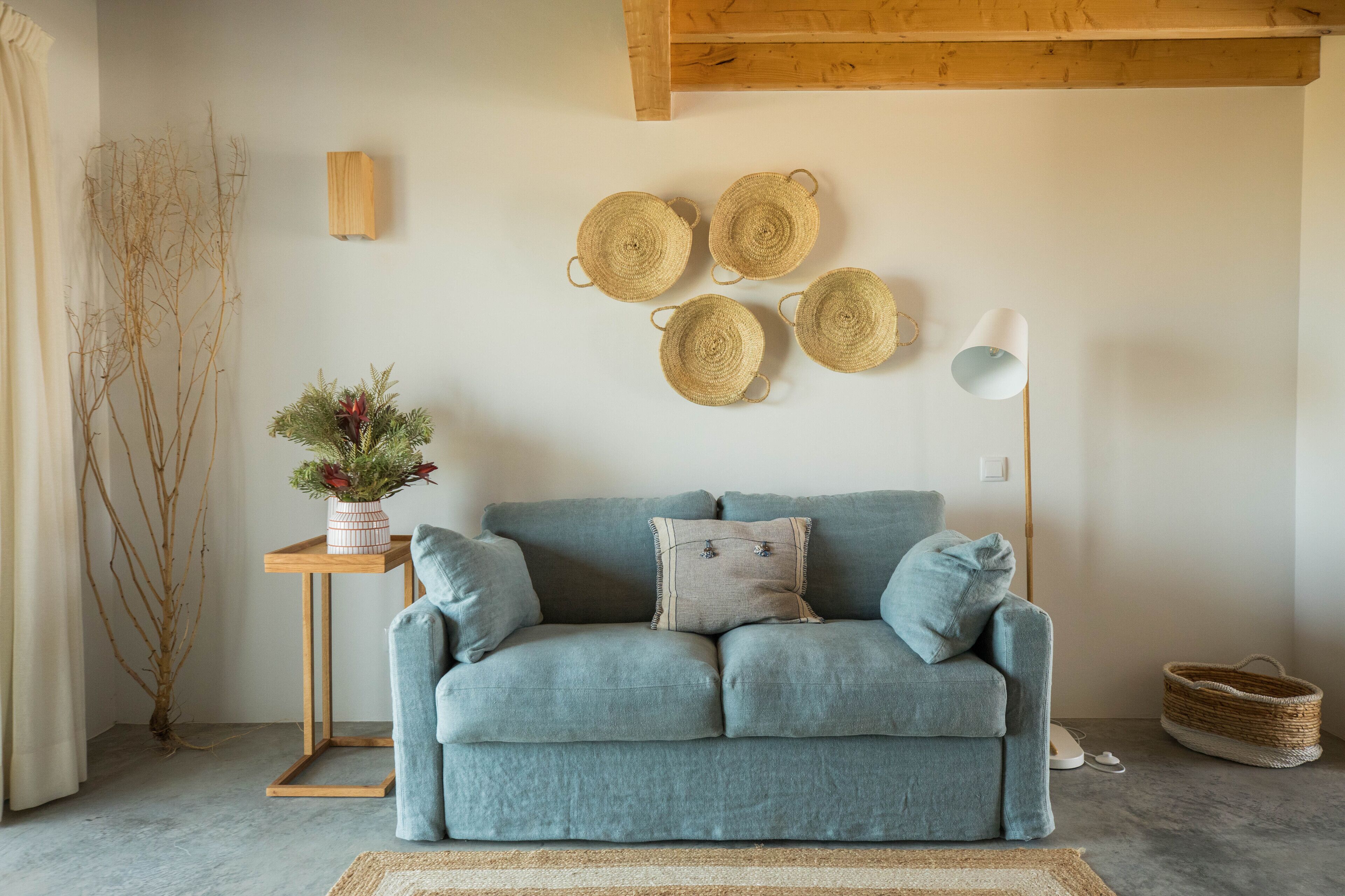 A cozy living room with a blue sofa, a small wooden side table with a vase of flowers, and a floor lamp.