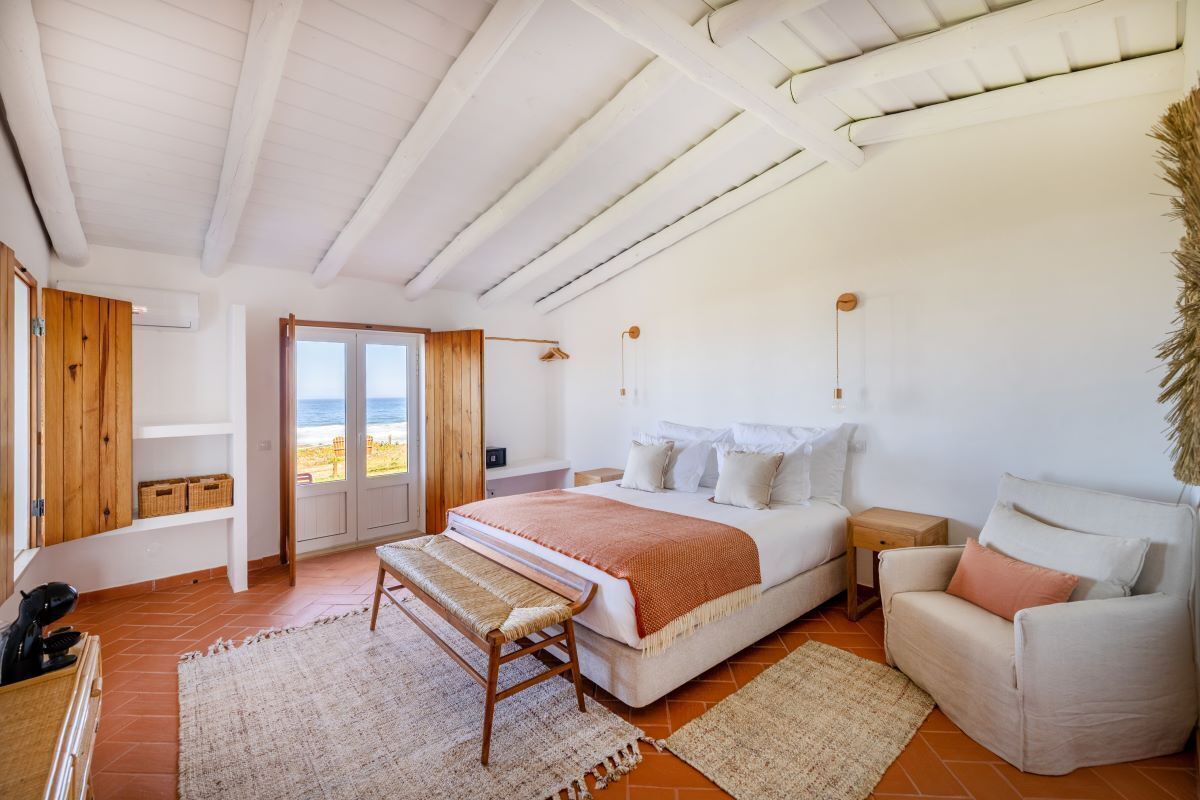 Un dormitorio con una cama grande, un banco, un sofá y vistas al mar.