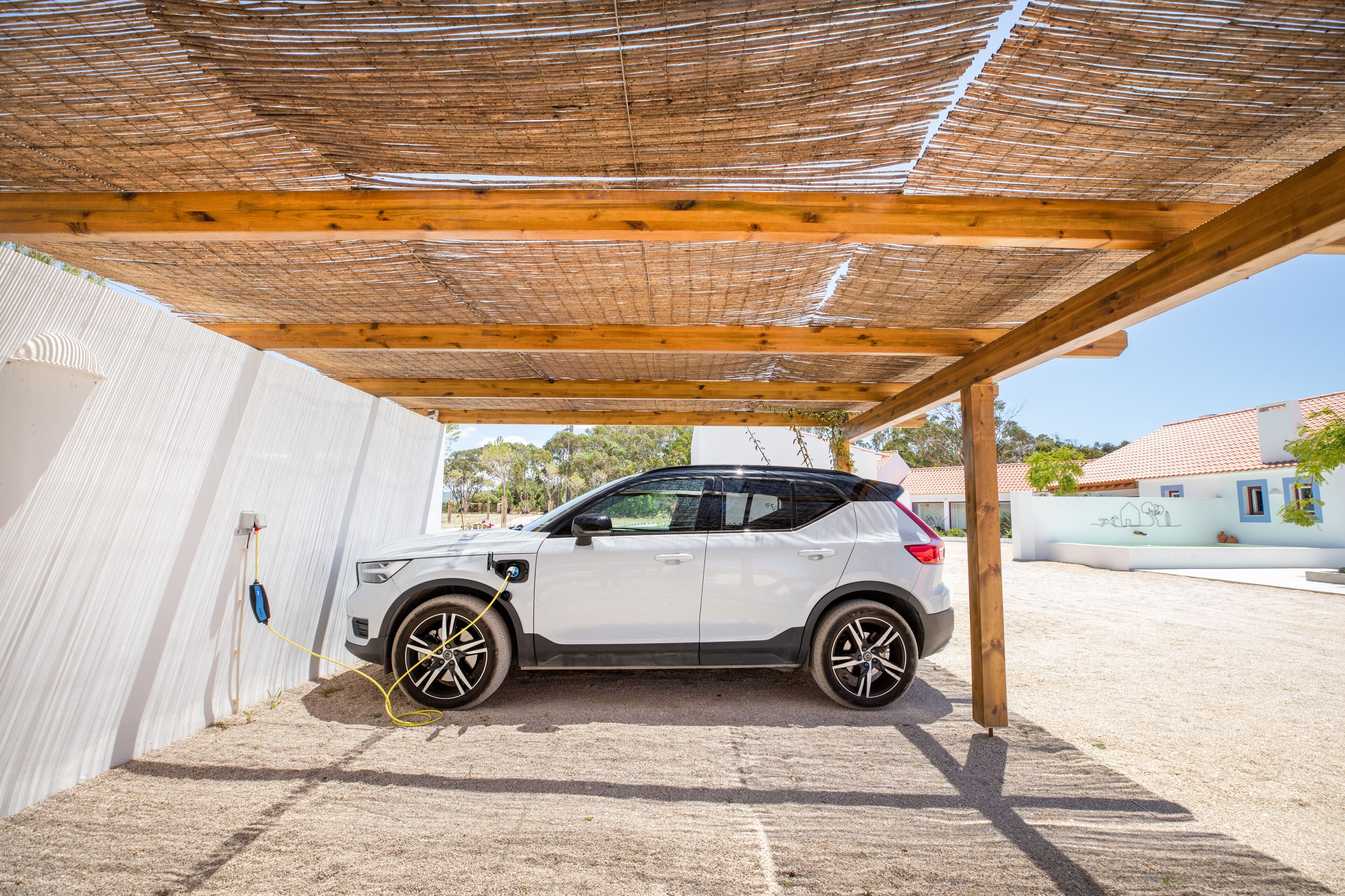 En hvid SUV parkeret under et træbeklædt pergola i et overdækket parkeringsområde.