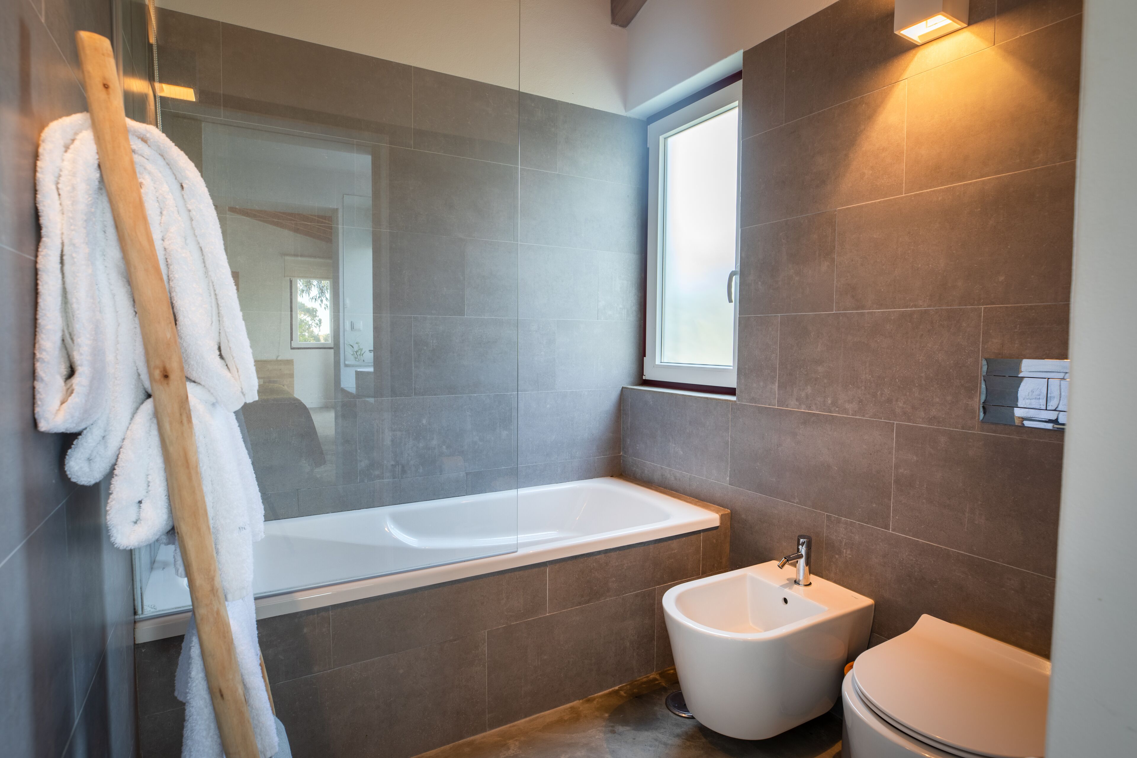 Un baño moderno con una bañera de hidromasaje con mampara de vidrio, un bidé y un inodoro blanco.