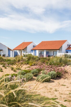A row of white buildings with red-tiled roofs, surrounded by sandy terrain and sparse vegetation.