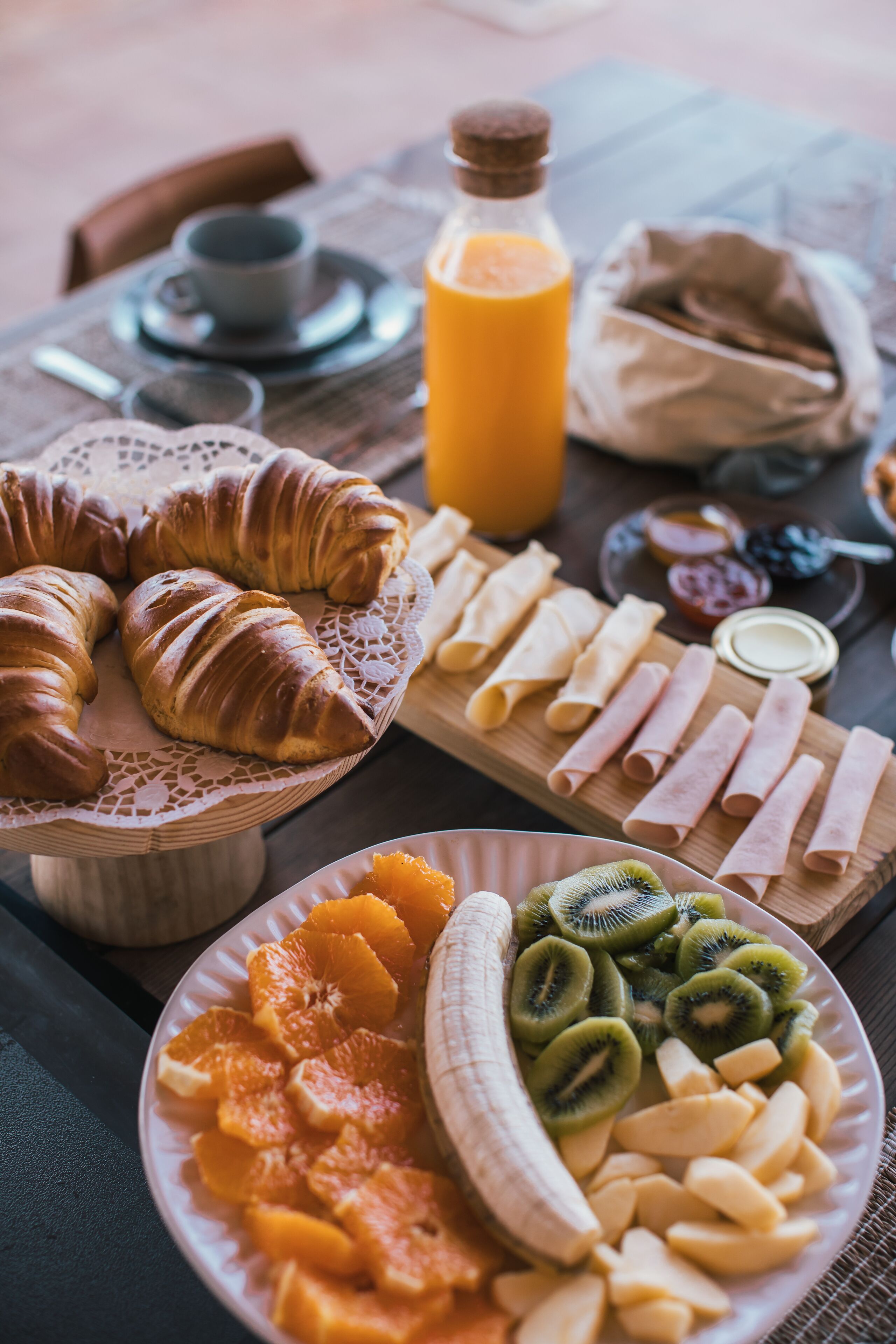 A breakfast spread with croissants, fruit, and jam on a wooden table.