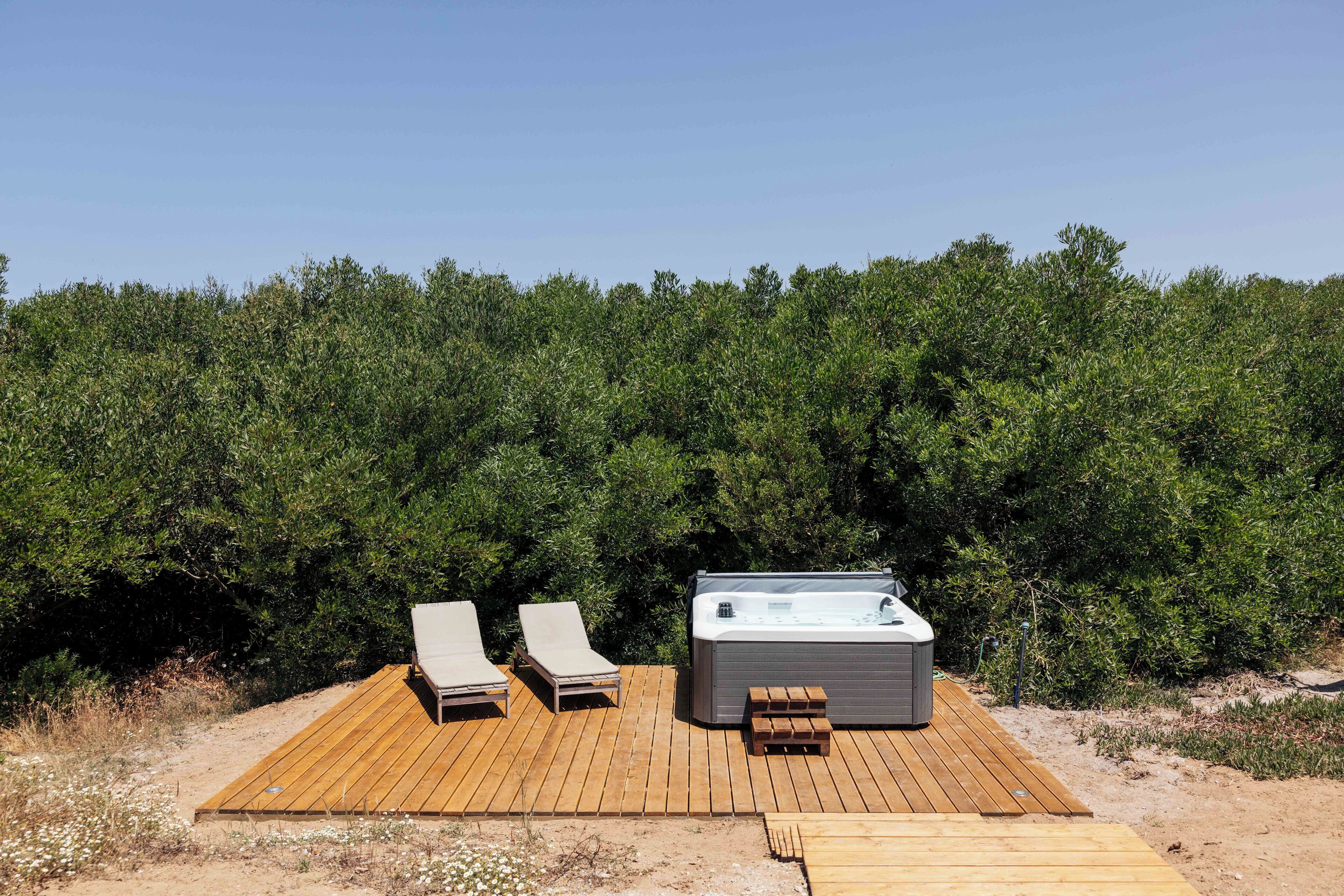 A wooden deck with two lounge chairs and a hot tub.